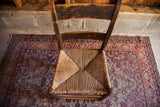 Antique chair's woven rush seat and aged wood backrest with visible cracks.