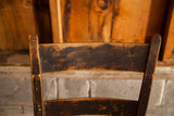 Close-up of dark wood back on antique chair, showcasing aged patina and top cracks.