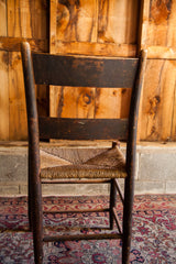 Dark wood leg with rich patina, and woven rush seat of antique chair over ornate Kerman rug.