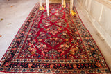 Close-up of semi-antique painted Sarouk runner, featuring dense ruby red floral field and dark blue border.