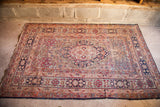 Antique Kerman rug corner with faded cochineal, dark blue florals, and visible wear.