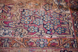 Detail of antique Kerman rug's worn texture, showcasing cochineal red, ivory, and blue floral motifs.