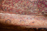 Close-up of the antique Kerman rug's tattered ends, revealing cochineal red and ivory floral motifs.
