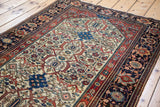 Antique Farahan Sarouk rug angled to show its detailed ivory field and deep blue border.