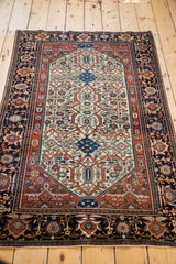 Angled full view of an antique Farahan Sarouk rug's ivory field and deep navy blue border.