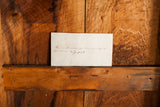 Handwritten ink note on aged off-white paper against natural wood.