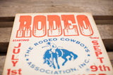 Vintage Mid Century Rodeo Poster showing aged red 'RODEO' text and blue cowboy graphic.
