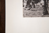 Detail of mounted black and white Native American dance photograph, showing ceremonial legwear and dirt ground.
