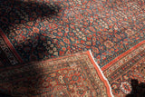 Antique Persian carpet's folded corner shows fringe, madder red border, and teal allover pomegranate field.