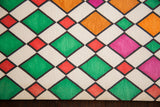 Textured vintage Harlequin art detail, showing green, red, orange, pink geometric diamonds.