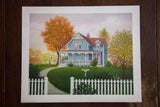 K Chin lithograph of a quaint blue house with a white picket fence during autumn.