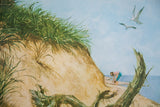 A woman collecting shells on the beach below a grassy dune and flying seagulls.