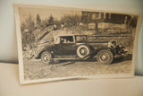 Angled view of sepia-toned antique car photograph with woman, dog, and curled edges.