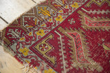 Historic Turkish mat's worn edge, geometric border, and aged red field with olive and yellow motifs.