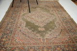 Intricate motifs and worn pile on the green field and red-toned border of the Turkish silk rug.