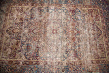 Antique Kerman rug with indigo medallion, ruby motifs, cloudband border, and central wear.