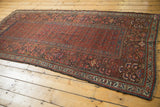 Antique Kurdish runner's time-softened red field, repeating boteh, and intricate borders.