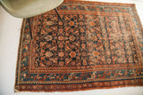 Tattered edge of vintage Persian Hamadan rug with dark blue Herati design and teal border.
