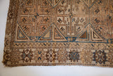 Aged geometric tribal patterns in brown, ivory, and blue from an antique Caucasian rug.