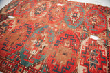 Bohemian tribal rug with repeating red and teal pomegranate motifs, showing wear and holes.