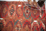 Old tribal rug with vibrant red and teal stylized pomegranate motifs, visible wear, holes, and tatter, 3'10