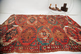 Repeating geometric tribal patterns in muted red and teal, showing evident holes and heavy wear.