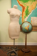 Mid-century dress form with discolored canvas cover, visible string tie, and metal stand.