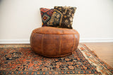 Antique leather pouf ottoman with dark orangey patina and embossed panel designs.