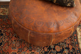 Embossed fan motifs and rich aged patina on the antique dark orangey leather pouf.