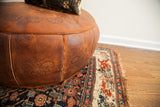 Patinaed dark orangey leather pouf with embossed motifs, on an antique Bijar rug.