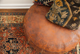 Rich dark orange leather of the antique pouf with decorative embossed motifs and patina.