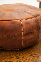 Embossed floral designs and hand-stitching on the rich orangey antique leather pouf.