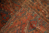 Tattered edge of antique Beshir rug, revealing worn brick red and distinct blue guls.