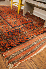 Antique Belouch rug's time-softened red and blue geometric design, showing the striped kilim end.