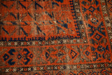 Time-softened rich burnt orange and deep blue geometric patterns on an antique Belouch rug.