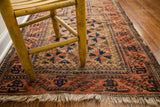 Soft walnut brown geometric field, peachy brick red border, and natural fringe on antique Belouch rug.