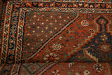 Rolled antique tribal Shiraz rug displays bold pinwheel and serrated leaf motifs.
