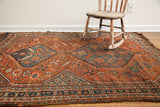 Angled view of an antique tribal Shiraz rug's detailed blue medallion, red field, and serrated motifs.