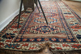 Antique Kazak runner end displaying geometric patterns, blue, red, and visible frayed fringe.