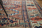 Geometric tribal motifs on an antique Kazak runner in rust, blue, and muted cream.