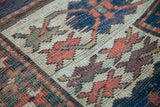 Hand-knotted tribal geometric patterns in aubergine, red, blue, and green on an antique Kazak rug.