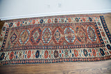 Antique Kazak runner end detail, geometric patterns in red, blue, and aubergine with wear.