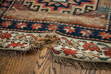 Torn edge of an antique Kazak runner showing geometric motifs and frayed fringe.