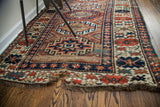 Storied end of antique Kazak rug with geometric borders, red, blue, and beige fringe.