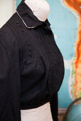 Textured black fabric, decorative buttons, and gathered waist of the Edwardian bodice.