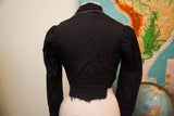Rear view of antique Edwardian black button bodice, showing gathered sleeves and raw lower hem.