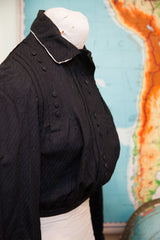 Edwardian black bodice, highlighting textured fabric, vertical buttons, and white collar trim.
