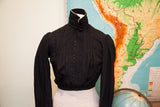 Antique Edwardian black button bodice with high collar and textured long sleeves.