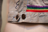Textured rainbow hand-stitching on the worn hem of a vintage jean jacket.