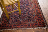 Vintage tribal Belouch rug corner, displaying madder red border, indigo field, and secure fringe.